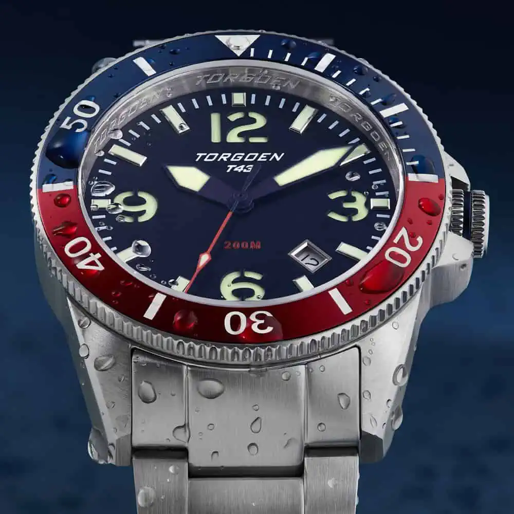 Detailed closeup of a steel watch in sparkling water drops with a vibrant blue red rim featured in a lifestyle product photographer showcase after