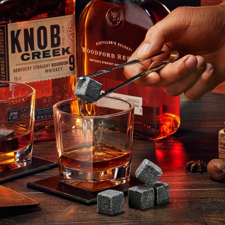 Hand placing cooling stones in whiskey glass wooden and amber tones bottles nuts spices in lifestyle product photographer