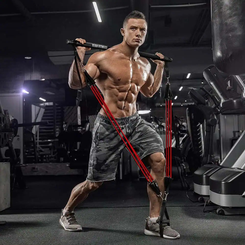 Young muscular man doing exercises with resistance bands against a dark gym background in advertising photography after